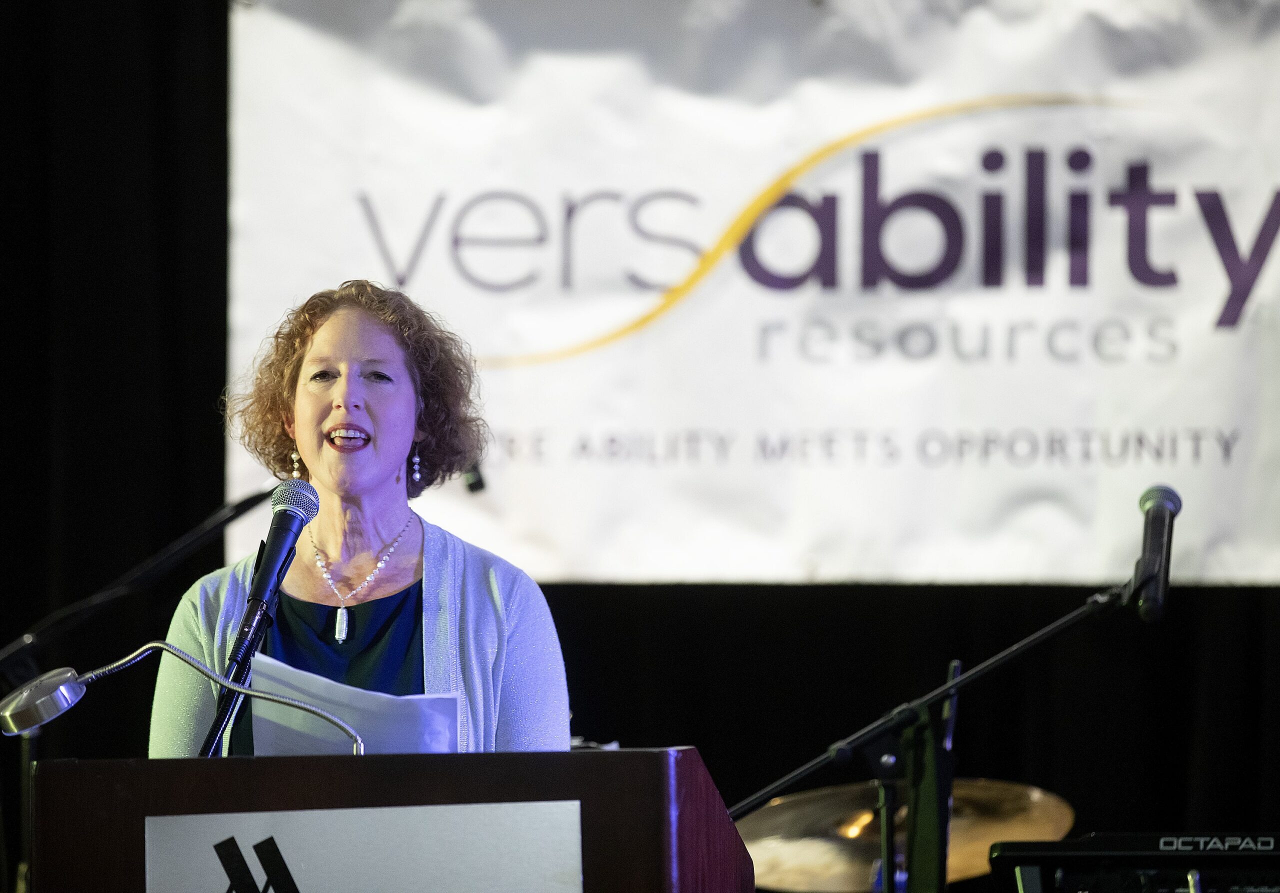 A woman wearing formal attire speaks into a microphone from a podium.