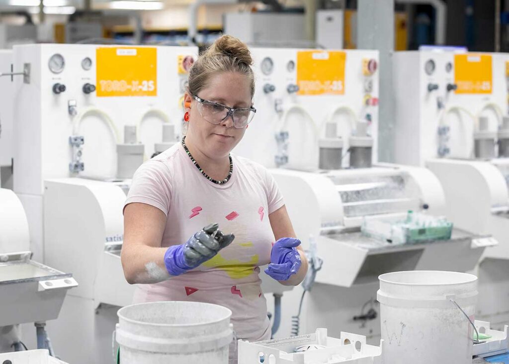 A woman wearing safety goggles and gloves making eyeglasses for the military at the Yorktown Naval Weapons Station