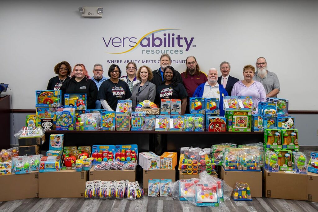 VersAbility members stand and smile behind toys from the Hampton Moose Lodge toy donation