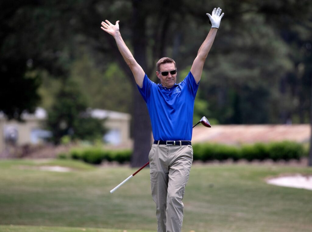 A man in golf attire throwing his hands in the air with his club behind him