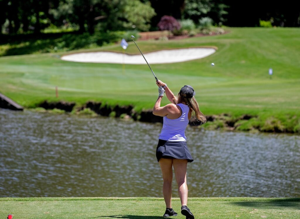 A woman hits a golf ball with a club over a lake on a golf course.