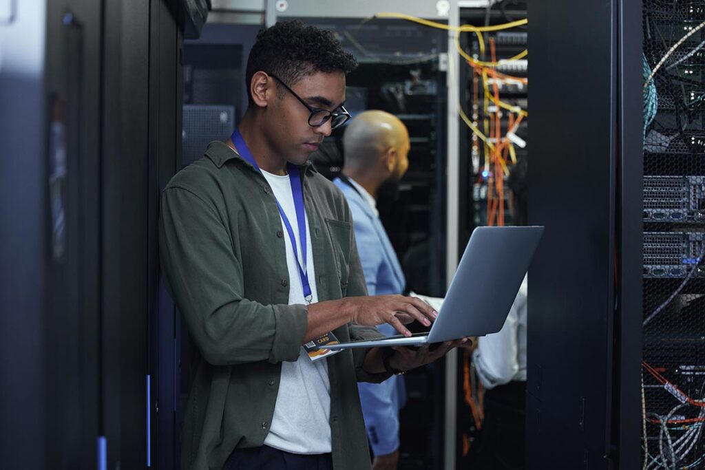 two male IT support agents working together in a dark network server room.