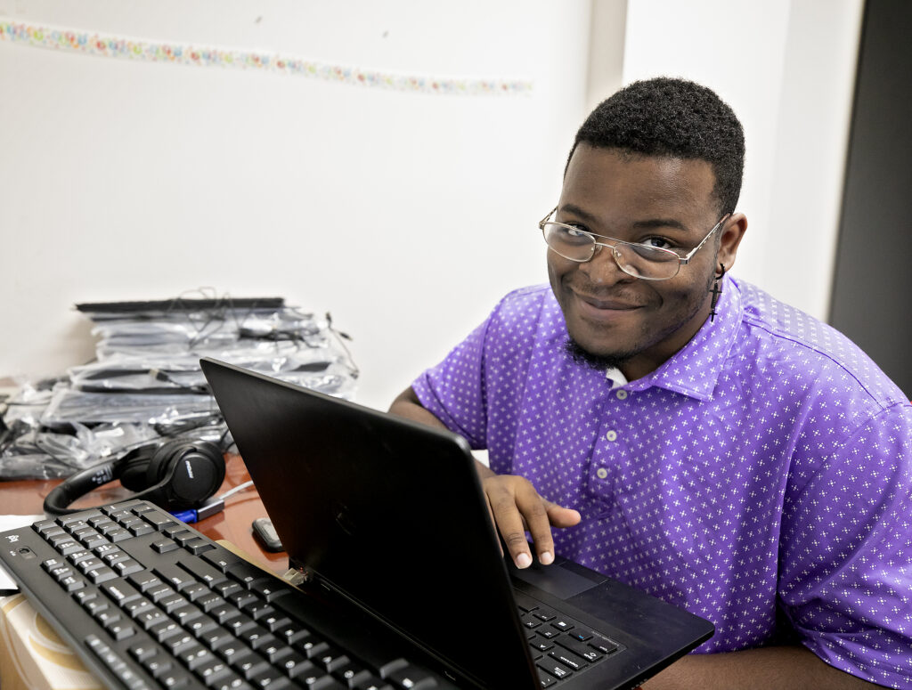 Man smiles from behind computer. 
