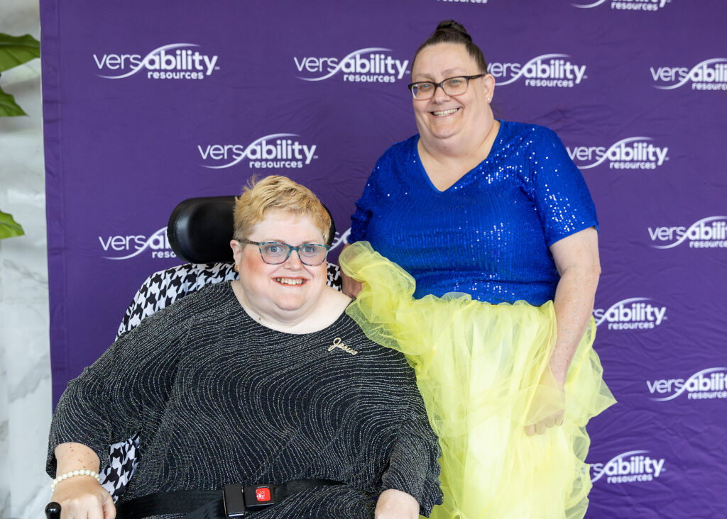 Two women smiling at the camera in front of VersAbility Resources backdrop
