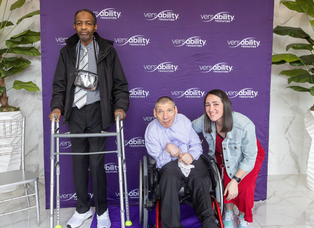 Three people smiling for the camera in front of VersAbility Resources backdrop