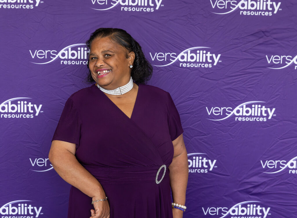 Woman in purple dress smiling for the camera in front of VersAbility Resources background 