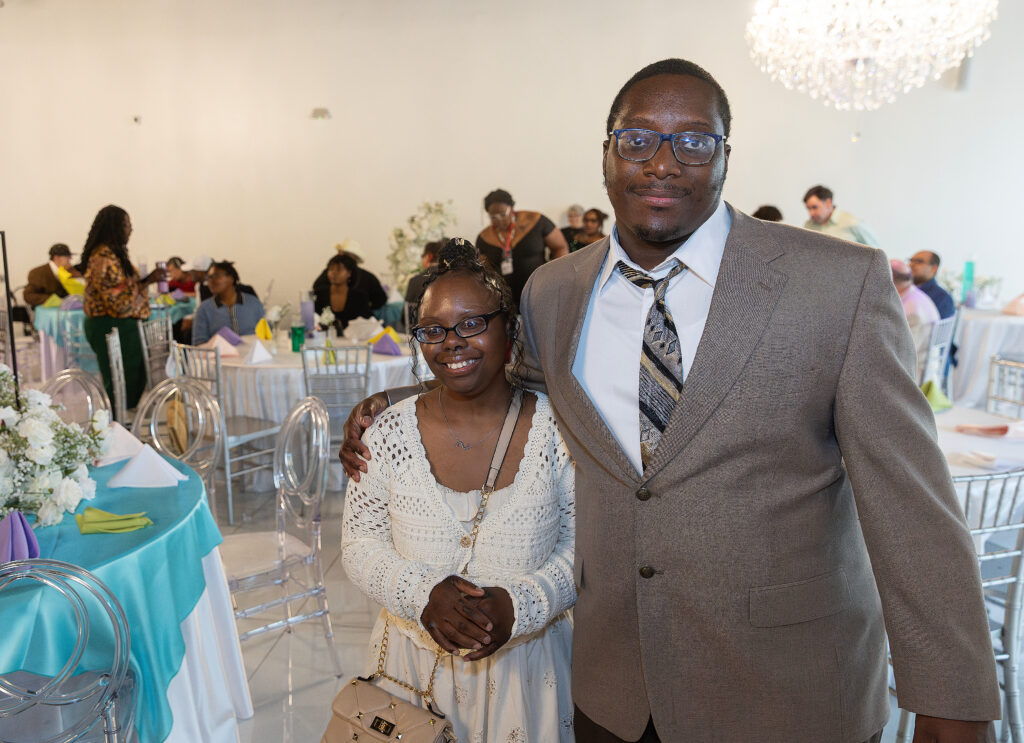 A man in a brown suit and a woman in a white dress smiling for the camera.