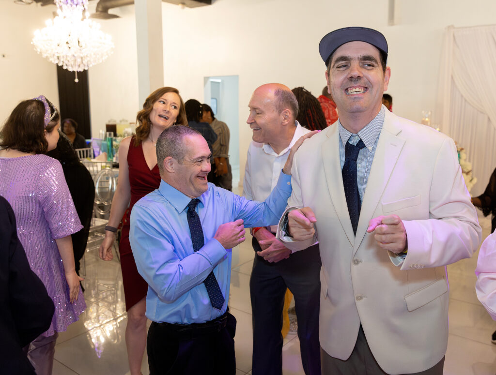 A group of friends in suits and dresses smile and dance together