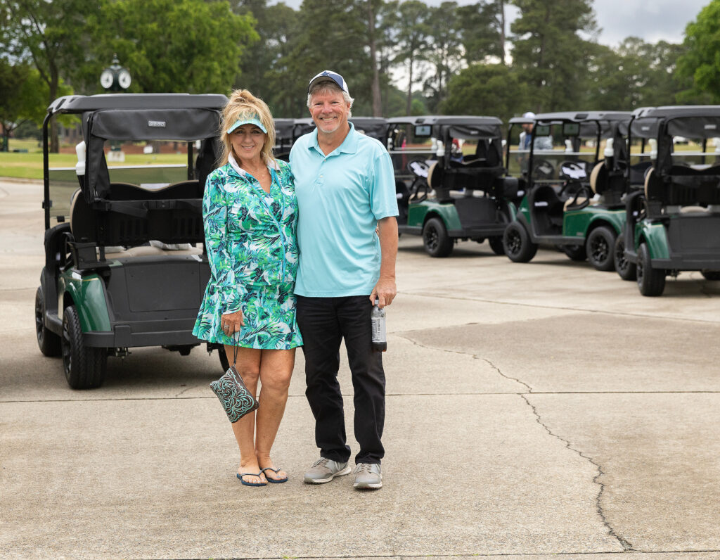 A couple poses happily at the VersAbility golf tournament, with golf carts lined up behind them.