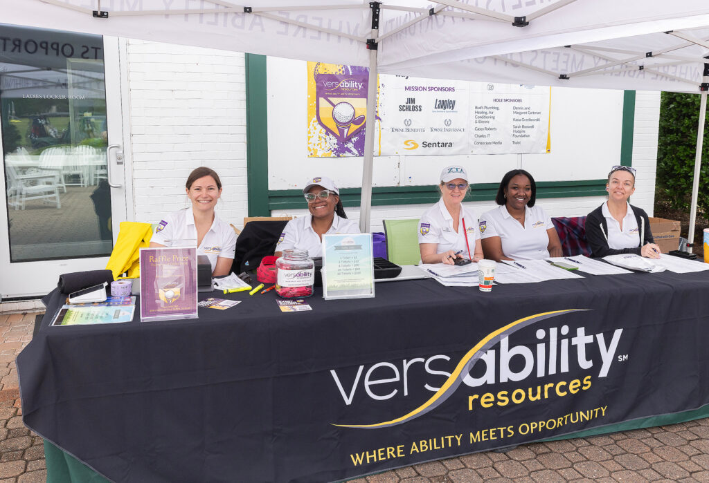 Staff at VersAbility golf tournament registration table, smiling and ready to assist participants with event details.