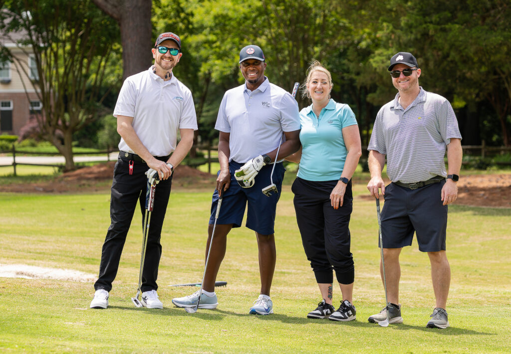 Golfers pose on a sunny green at the VersAbility golf tournament, showcasing camaraderie and sportsmanship.